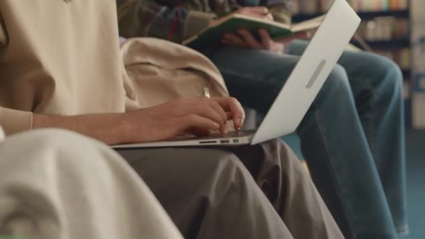 Detailní náklon záběr mladého Araba sedícího v univerzitní knihovně, psaní na notebooku při práci na diplomové práci, diskuse o úkolu s bělošským přítelem, který se dívá na obrazovku a dělá si poznámky - Záběry, video