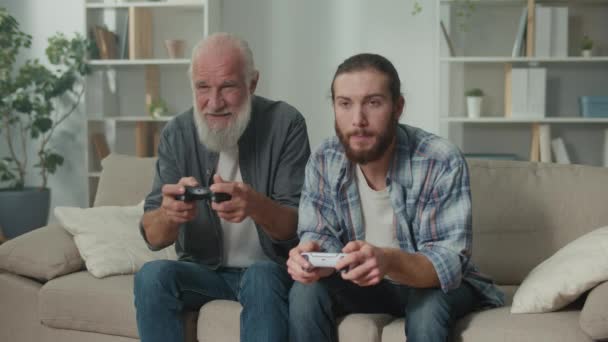 Jonge en oudere man gelukkig tijd doorbrengen met het spelen van een computerspel met joysticks, lachen en genieten van het spel, cross-generationele communicatie, entertainment technologie, familie interactie - Video