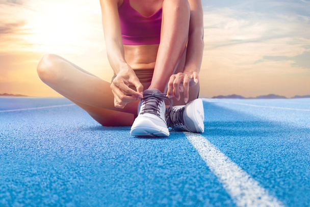 Afroamerykanka atletka, kobieta z bliska sznuruje buty siedząc na niebieskim torze olimpijskim, ucieleśniając koncepcję treningu wyścigowego i poświęcenia w sporcie, biegając codziennie - Zdjęcie, obraz