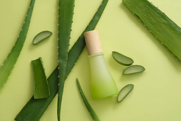 Against a light background, Aloe vera leaves and a jar with wooden cap are displayed. Beauty cosmetic product with empty label for mockup design of Aloe vera (Aloe barbadensis miller) extract - Photo, Image