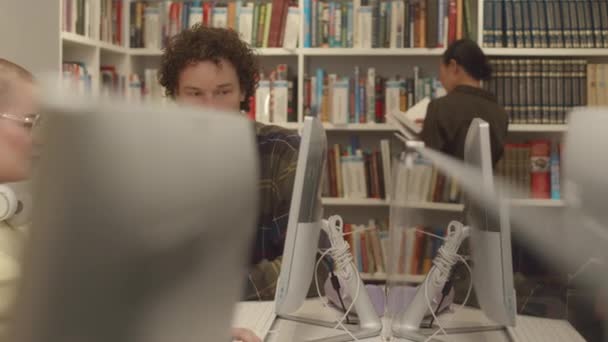 若い白人男性と女性がデスクトップコンピュータの前に座ってインターネットを閲覧し,割り当てを準備し,タスクを議論し,メモを取る - 映像、動画