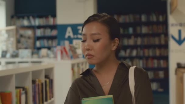 Detailní záběr záběr krásné mladé asijské ženy se stresem a starosti o tvář odchodu z knihovny po vyjmutí knihy připravit na univerzitní zkoušky - Záběry, video