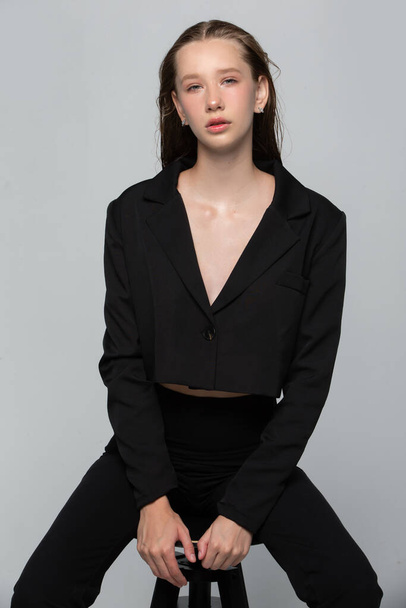 Menina fina bonita em uma jaqueta preta em um fundo cinza. - Foto, Imagem