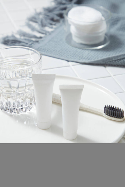 Eine runde Schüssel mit einem Glas Wasser, einem nicht etikettierten Schlauch und einer Zahnbürste darauf. Bio-Produkt-Attrappe. Aloe Vera (Aloe barbadensis miller) hilft, schädliche Bakterien im Mund zu beseitigen - Foto, Bild