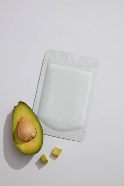 Eine halbe Avocado dekoriert mit einem Maskentuch mit leerem Etikett für Branding-Attrappen. Gesichtsmaske aus Avocado (Persea americana) kann Akne behandeln und die Haut mit Feuchtigkeit versorgen - Foto, Bild