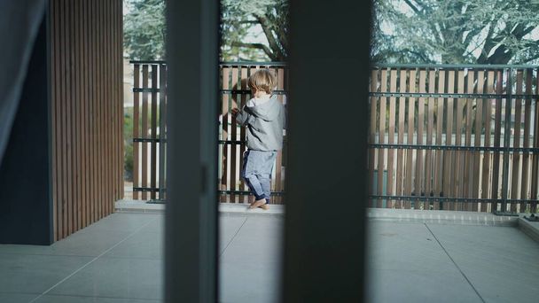 Niño pequeño abriendo la puerta al balcón del apartamento. Niño yendo a casa terraza apoyado en la barrera - Foto, Imagen