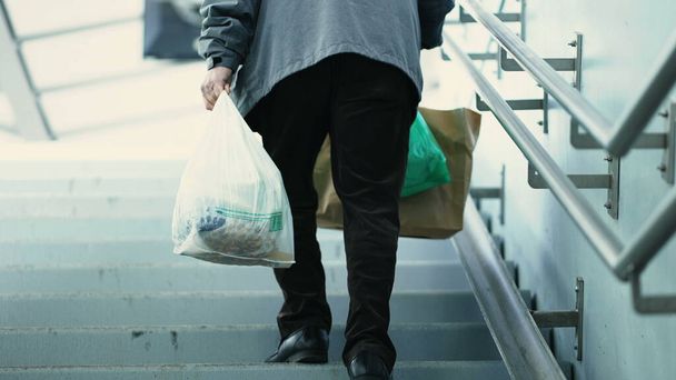 Человек, несущий продукты вверх по лестнице от подземного поезда. Ежедневный пригородный с продуктами восходящие лестницы от метро - Фото, изображение