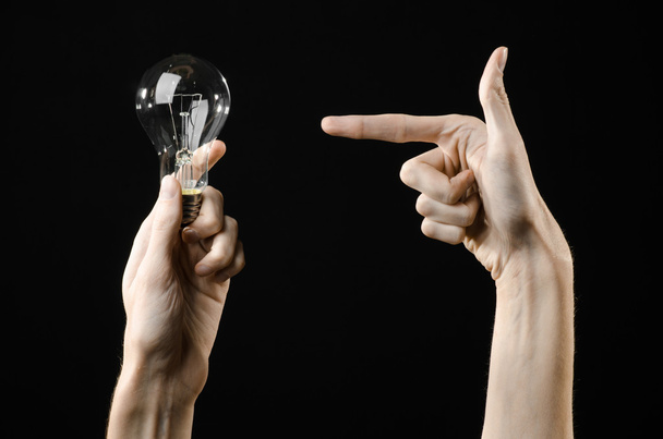 エネルギー消費量と省エネルギーのトピック: studio で黒い背景に電球を保持している人間の手 - 写真・画像