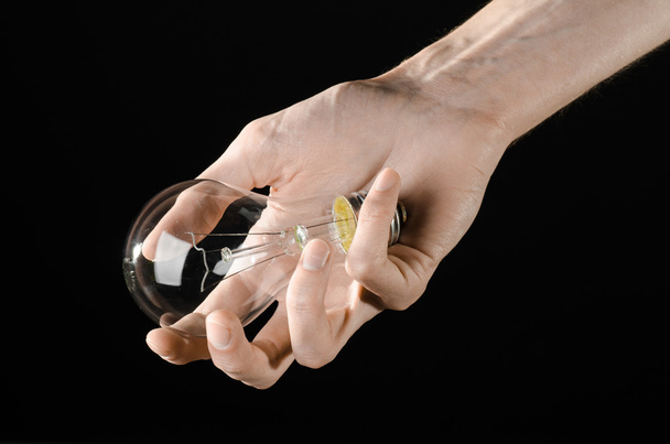 Energy consumption and energy saving topic: human hand holding a light bulb on black background in studio - Foto, Imagem