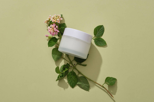 Valkoinen kosmeettinen purkki ilman etikettiä näytetään Lantana camara kukkia. Säiliö pakkaus ihonhoito brändäys Lantana camara kukkia ote - Valokuva, kuva