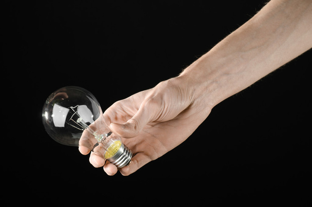 Energy consumption and energy saving topic: human hand holding a light bulb on black background in studio - Zdjęcie, obraz