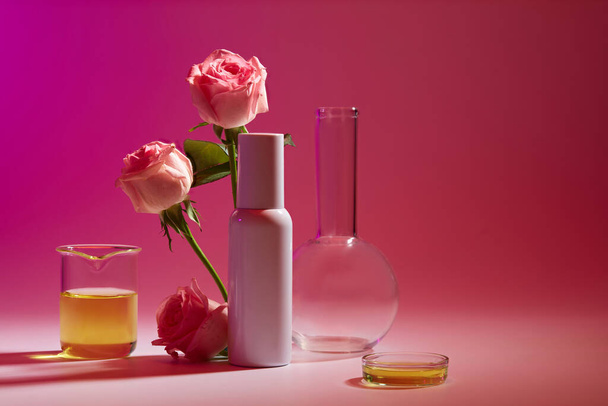Widok z przodu w laboratorium z pustą butelką etykiety ozdobioną gałązkami róży i szklanymi naczyniami. Odbiór. Koncepcja produktów kosmetycznych - Zdjęcie, obraz