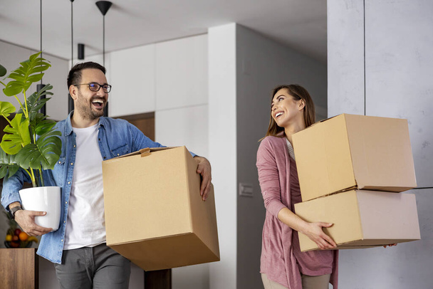 Young couple carry cardboard boxes into their new home where they were moving in together. Happy family with cardboard boxes.  - Photo, Image