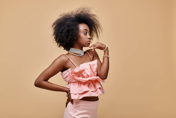 довольно африканская американская девушка в возрасте 20 лет позирует в персиковой оборке и пастельной юбке с рукой на бедре - Фото, изображение