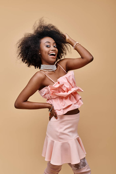 excited african american girl in 20s posing in peach ruffle top and pastel skirt with hand on hip - Photo, Image