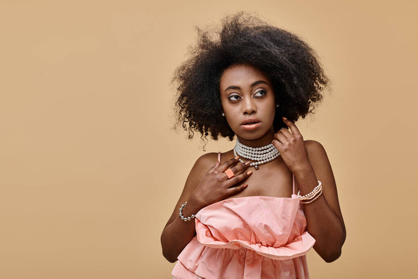 fiatal sötét bőrű nő göndör haj pózol pasztell barack fodros tetején bézs háttér - Fotó, kép