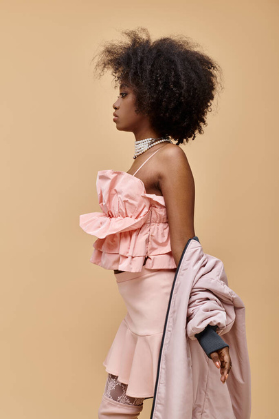 göndör afro-amerikai nő pózol pasztell ruhát dzseki bézs háttér, barack fuzz - Fotó, kép