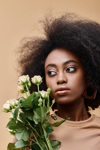 young and curly african american woman holding tiny flowers on beige background, peach fuzz color - Foto, afbeelding
