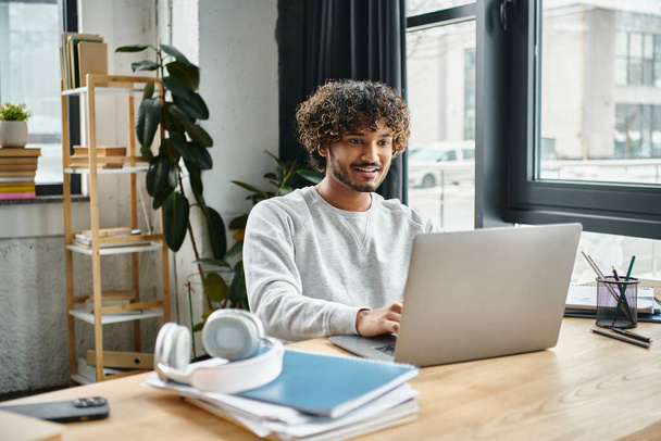 Ein Mann mit unterschiedlichen kulturellen Hintergründen sitzt an einem Laptop in einem Coworking Space, konzentriert und mit seiner digitalen Arbeit beschäftigt. - Foto, Bild