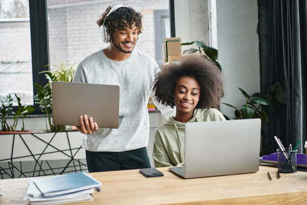 Um homem e uma mulher multicultural focados em laptops, colaborando em um moderno espaço de coworking de escritório. - Foto, Imagem
