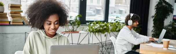 Una mujer de ascendencia diversa se sienta en un profundo pensamiento frente a una computadora portátil, inmersa en el trabajo o el estudio, en un moderno espacio de coworking. - Foto, imagen