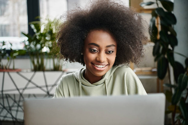 Eine schwarze Frau, die in der Arbeit versunken vor einem Laptop in einem modernen Coworking Space sitzt. - Foto, Bild