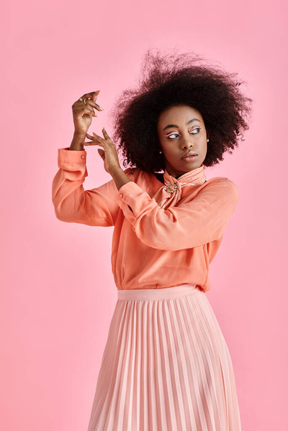 молода афроамериканка в персиковій блузці, спідниці та шарфі позує на пастельному рожевому фоні - Фото, зображення