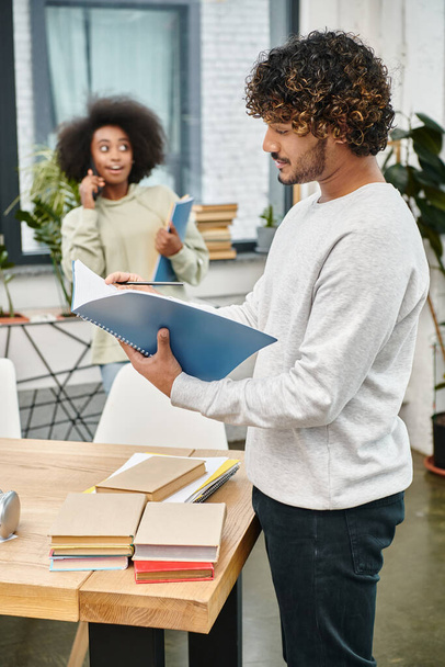Egy ember áll az asztal előtt, kezében egy iratgyűjtővel, elmerülve a tanulmányaiban egy modern coworking térben, amit technológia vesz körül.. - Fotó, kép