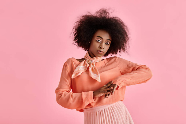 pretty african american woman in peach blouse, midi skirt and neck scarf posing on pink backdrop - Photo, Image