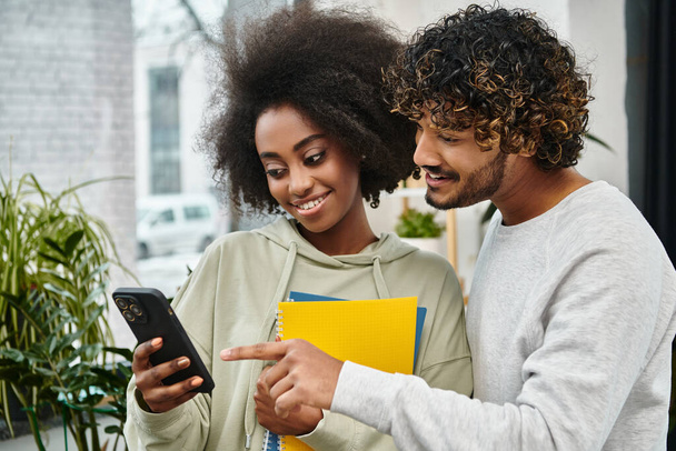 Um homem e uma mulher multicultural envolvidos na visualização de conteúdo em um telefone celular em um moderno espaço de coworking. - Foto, Imagem
