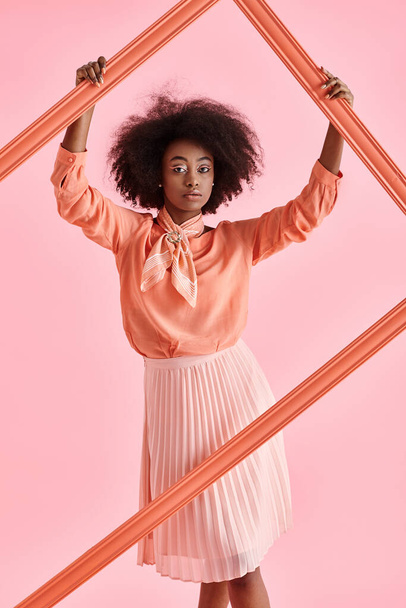 bonita mujer afroamericana en blusa de pelusa de melocotón y falda midi posando en marco sobre fondo rosa - Foto, imagen