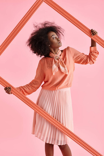 chica afroamericana de ensueño en blusa de pelusa de melocotón y falda midi posando en marco sobre fondo rosa - Foto, imagen