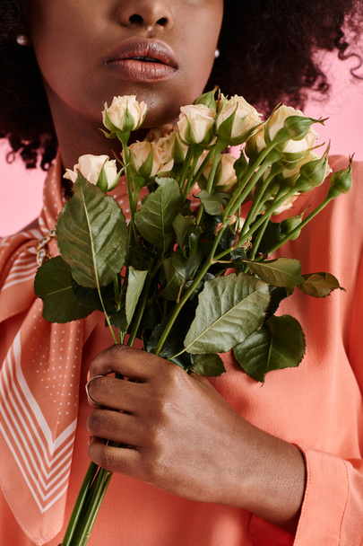 przycięty widok afrykańskiej dziewczyny w brzoskwiniowej bluzce fuzz gospodarstwa kwiaty na różowym tle - Zdjęcie, obraz