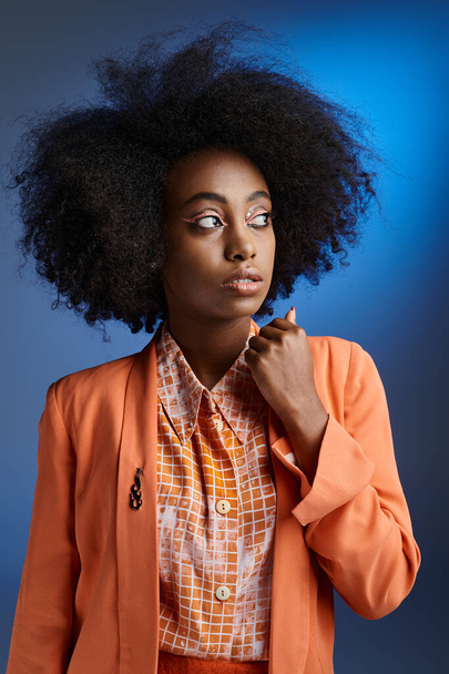 encaracolado jovem afro-americano mulher em pêssego fuzz blazer olhando para longe no gradiente azul pano de fundo - Foto, Imagem