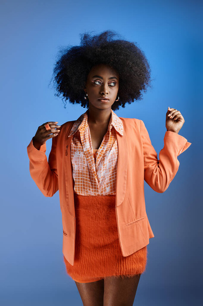 curly african american woman in peach fuzz outfit with blazer looking away on gradient blue backdrop - Valokuva, kuva