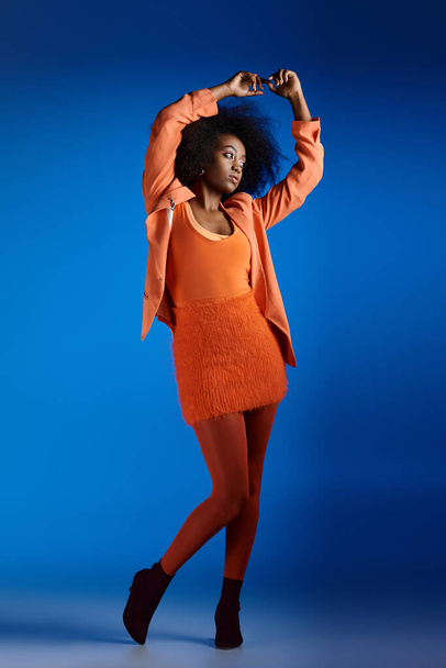 curly young african american model in textured dress and blazer posing with raised hand on blue - Photo, Image