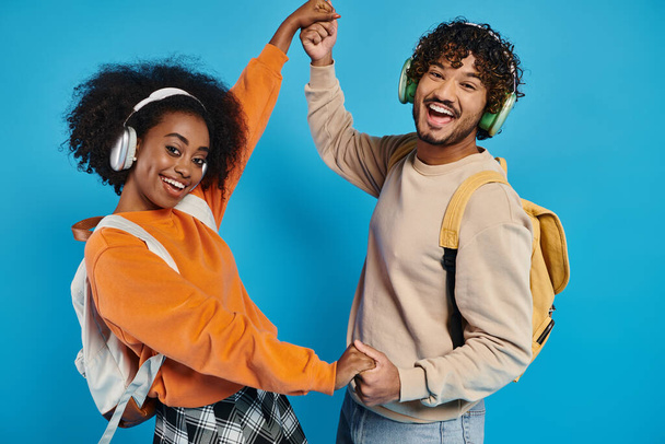Un hombre interracial y una mujer bailan juntos, usando auriculares, expresando alegría y conexión a través del movimiento sobre un telón de fondo azul. - Foto, imagen
