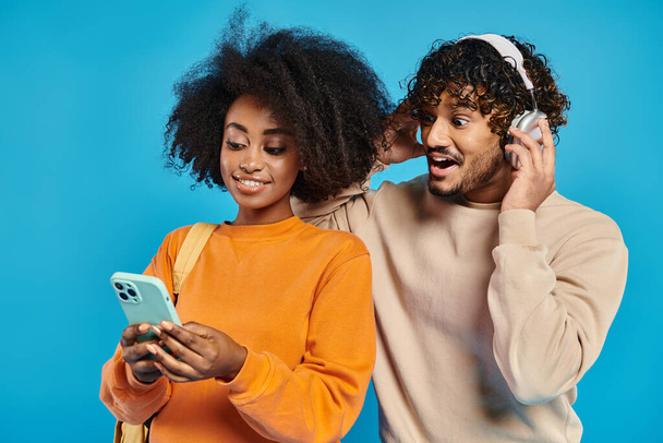 Un couple interracial en tenue décontractée debout ensemble, absorbé par la recherche d'un écran de téléphone portable. - Photo, image