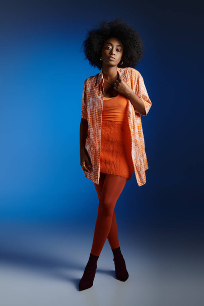 青い背景にパターンされたシャツとオレンジ色のドレスの美しいアフリカ系アメリカ人女性のシックな外観 - 写真・画像