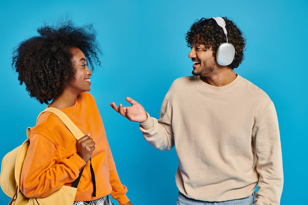 Two interracial students wearing casual attire stand confidently together against a blue backdrop in a studio setting. - Photo, Image