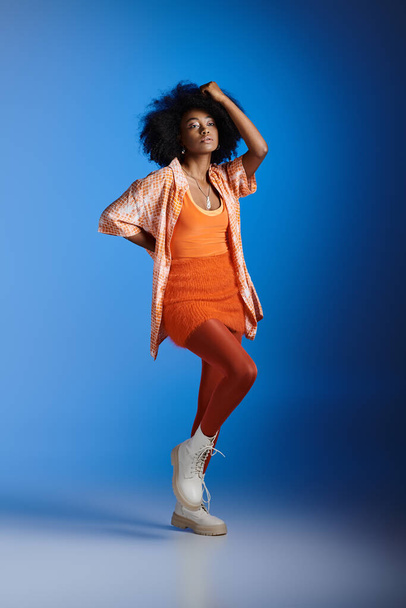stylowa Afroamerykanka we wzorzystej koszuli i teksturowanej sukience pozowanie na niebieskim tle - Zdjęcie, obraz
