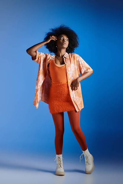 fashionable african american model in patterned shirt and textured dress posing on blue backdrop - Photo, Image