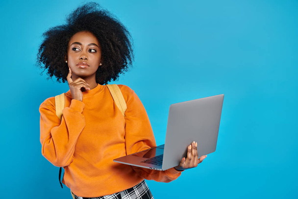 Африканська американська дівчина в повсякденному вбранні стоїть з ноутбуком перед синім тлом. - Фото, зображення