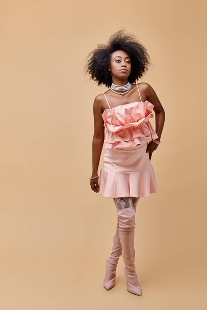 brunette young african american woman in peach ruffled top and over knee boots on beige background - Photo, Image
