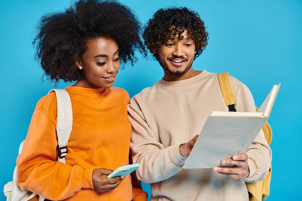 Un homme et une femme interracial debout, examinant un morceau de papier ensemble dans un cadre de studio sur un fond bleu. - Photo, image