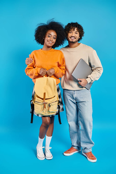 異人種間のカップルの学生がスタジオの青い背景に対してカジュアルな服装で一緒に立っています. - 写真・画像