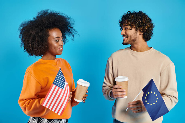 Ein gemischtrassiges Paar in legerer Kleidung steht zusammen und hält Kaffeetassen und Fahnen in der Hand - Foto, Bild