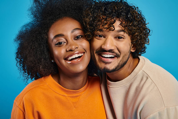 Een man en vrouw, die interraciale harmonie vertegenwoordigen, glimlachen helder in een studio met een blauwe achtergrond. - Foto, afbeelding