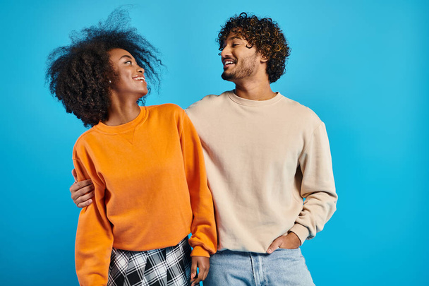 An African-American woman and indian man, both students, stand together in casual attire against a blue backdrop. - Foto, Bild