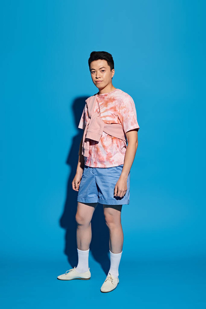 A trendy young man striking a dynamic pose in stylish attire against a vivid blue background. - Foto, imagen